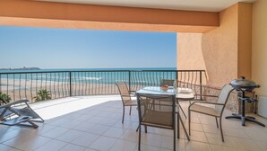 Een balkon met uitzicht op het strand en de oceaan, voorzien van een tafel, stoelen en een barbecue.