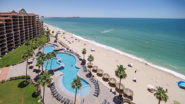 Un resort con un'ampia area piscina, una spiaggia e l'edificio dell'hotel.