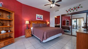 Una habitación de hotel con una cama, una mesita de noche de madera, una lámpara, una cruz en la pared y un cuadro.