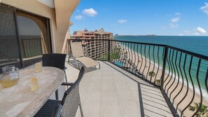 A balcony with a table and chairs, overlooking a beach and ocean.