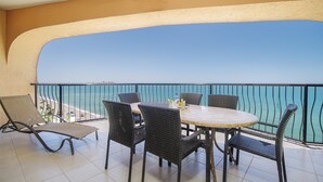 Un balcone con un tavolo rotondo e sei sedie in vimini, affacciato su una spiaggia e il mare.