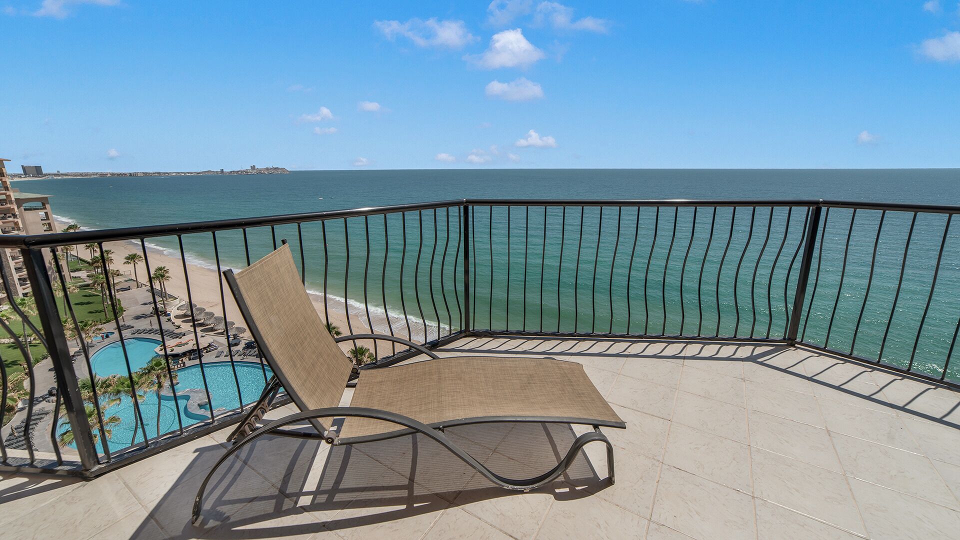 A balcony with a view of the ocean, a pool, and a beach area.