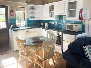 A kitchen with white cabinets, a microwave, and a sink. There is a fire blanket on the wall and a fire extinguisher.