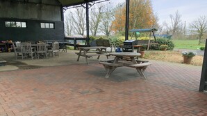 An outdoor patio area with brick flooring, picnic tables, and barbecue grills. - 2 bedroom accommodation in Near Ely (Near Ely)