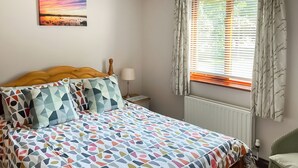 A bedroom with a bed, a nightstand, a lamp, a window with curtains, and a wall-mounted picture. - 2 bedroom accommodation in Near Ely (Near Ely)