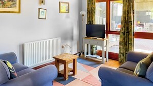 A living room with two blue sofas, a wooden coffee table, a TV on a stand, and a radiator. - 2 bedroom accommodation in Near Ely (Near Ely)