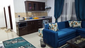 Cocina moderna con armarios oscuros, microondas y lavadora. Hay un sofá azul con cojines estampados y una mesa de centro.