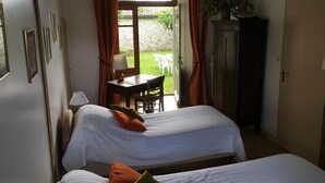A room with two beds, a desk with a chair, a lamp, and a view of a garden through an open door. - Logis near the chateau (Paizay-Naudouin-Embourie)