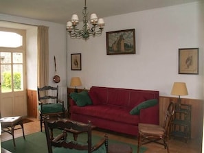 Een woonkamer met een rode bank, twee houten stoelen, een kroonluchter en ingelijste foto's aan de muur.