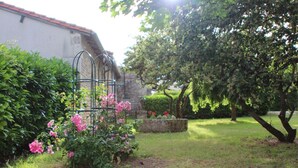 A garden with a metal trellis, flowering plants, and a stone planter. - Logis near the chateau (Paizay-Naudouin-Embourie)