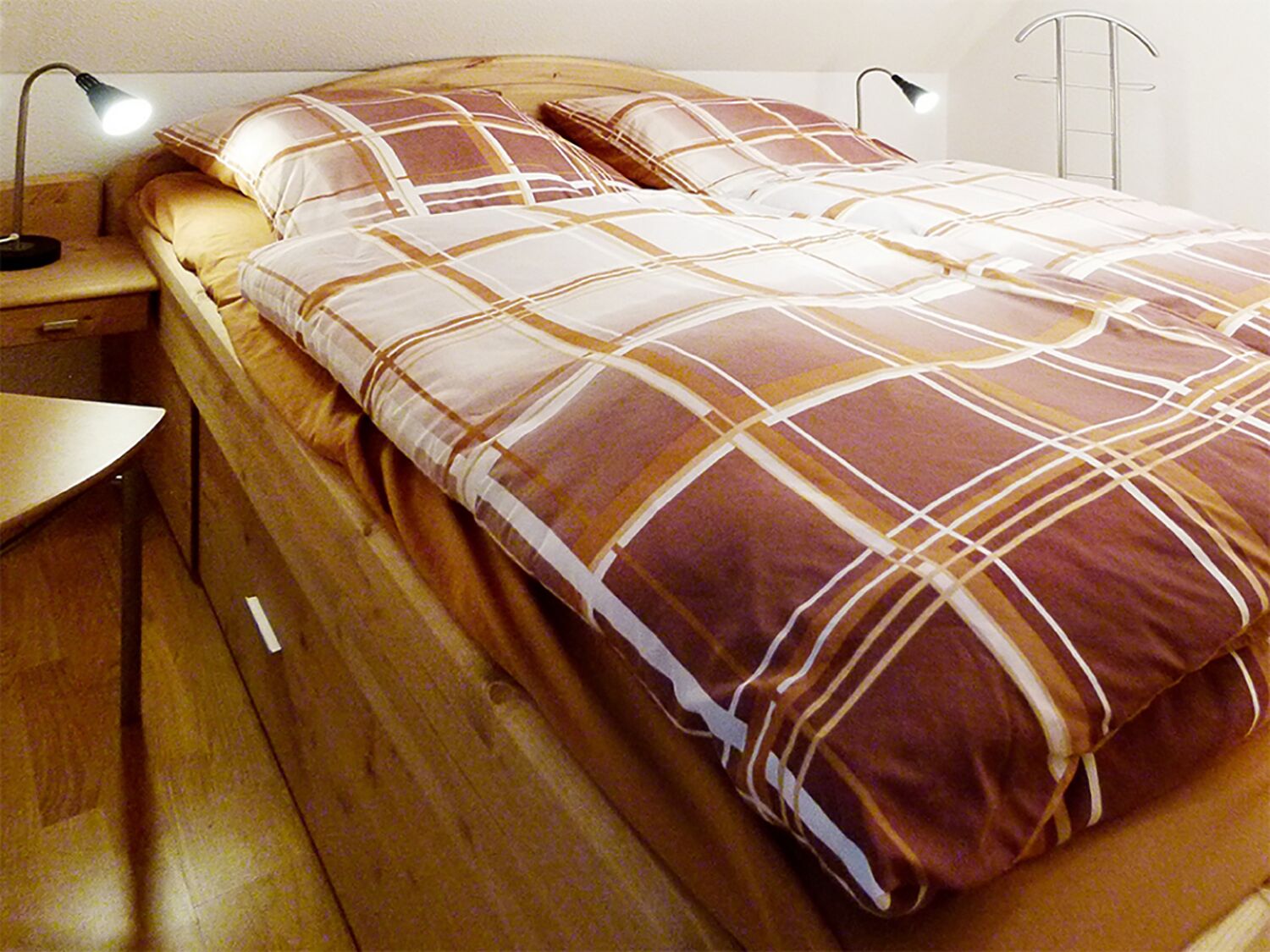 Un lit recouvert d’une couverture à carreaux, une table de chevet, une lampe et une échelle fixée au mur.