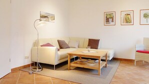 A modern living room with a white sofa, a wooden coffee table, and a floor lamp. There are three framed pictures on the wall and a small table with a glass. - cozy apartment near the Darßwald, beach chair on balcony, WiFi, 4 pers. (Prerow)