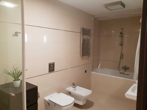 Bathroom features a glass-enclosed shower, handheld showerhead, towel rack, and separate toilet with bidet.