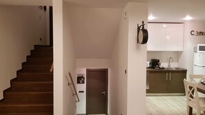 A modern apartment with a staircase leading to a second floor, a kitchen area with white cabinets and a dining table, and a door with a towel hanging on the wall. - Luxury  silver mountain resort (Poiana brasov)
