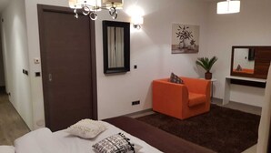 A hotel room with a bed, a brown door, a white wall, a brown rug, an orange sofa, a potted plant, a mirror, and a chandelier. - Luxury  silver mountain resort (Poiana brasov)