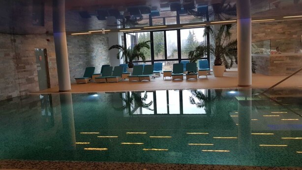 An indoor swimming pool with clear water, lounge chairs, and large windows. - Luxury  silver mountain resort (Poiana brasov)