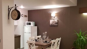 A dining area with a wooden table set for four, white chairs, a clock, a microwave, and a small potted plant. - Luxury  silver mountain resort (Poiana brasov)