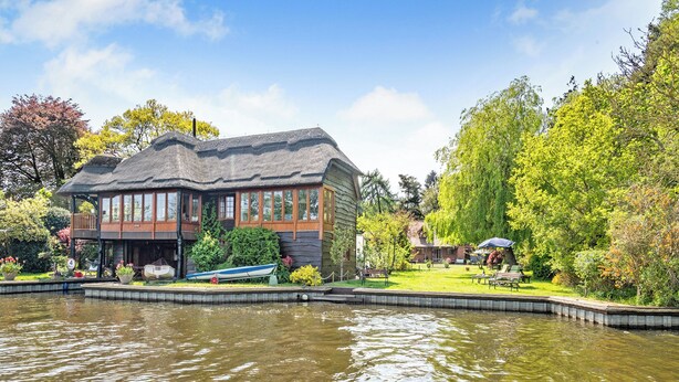 Un bâtiment situé au bord du lac, doté d’un quai, et entouré d’une végétation luxuriante et d’arbres.