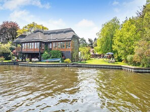 A lakeside building with a dock, surrounded by lush greenery and trees. - 4 bedroom accommodation in Irstead, near Wroxham (Irstead, near Wroxham)