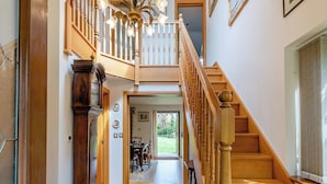 Un escalier en bois avec une rampe, un coin repas avec une table et des chaises, et une vue sur l’extérieur.
