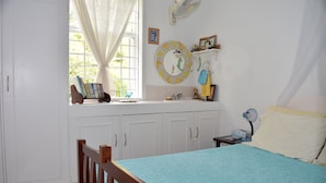 A bedroom with a bed, a window with curtains, a bedside table, a nightstand, and a wall-mounted fan. - Eco-friendly room in the Hummingbird apartment (St. Michael)
