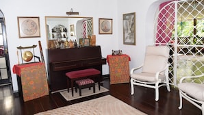 A living room with a piano, a white armchair, a bench, and a patterned rug. - Eco-friendly room in the Hummingbird apartment (St. Michael)
