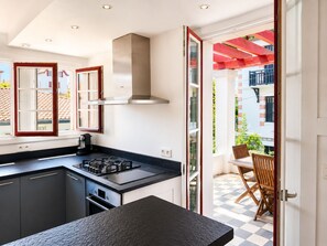 Uma cozinha moderna com fogão a gás, exaustor de aço inoxidável e área de jantar com chão xadrez e mobiliário de madeira.