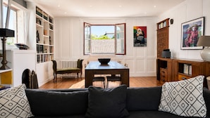 A living room with a sofa, dining table, chairs, a radiator, a bookshelf, and a window with an open door. - Architect-designed villa 200 m² 5 min from the beach (Saint-Jean-De-Luz)