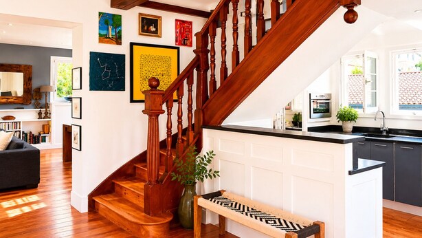 A wooden staircase with a bench, a kitchen with a black countertop, and a dining area with a sofa and bookshelves. - Architect-designed villa 200 m² 5 min from the beach (Saint-Jean-De-Luz)