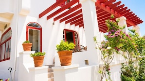 A white building with red accents, featuring a balcony with potted plants and a red pergola. - Architect-designed villa 200 m² 5 min from the beach (Saint-Jean-De-Luz)