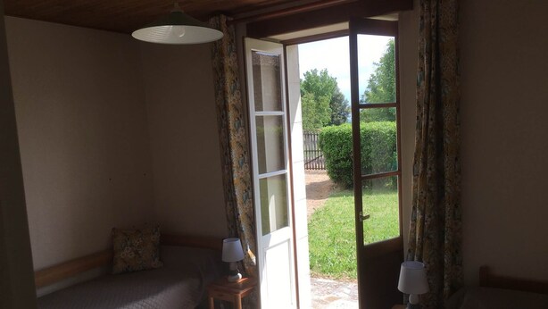 Una habitación acogedora con una cama, una mesita de noche con una lámpara y una puerta que da a un jardín.