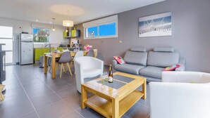 Ein modernes Wohnzimmer mit einem grauen Sofa, einem Holztisch und einem Essbereich mit Tisch und Stühlen.