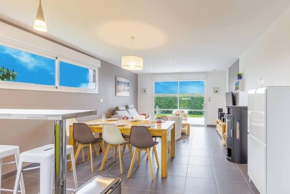 A modern kitchen with a dining area, large windows, and a view of greenery. - Villa Enora Bord de Mer : Pool 29°C, Private Spa & Beach and path 100m away (Sibiril)