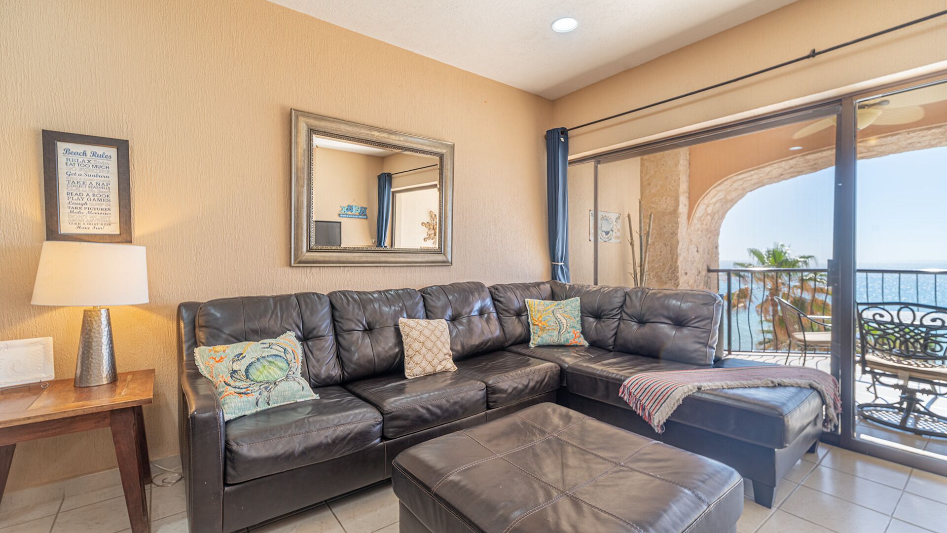 A living room with a leather sofa, a mirror, and a balcony with a view of the sea.
