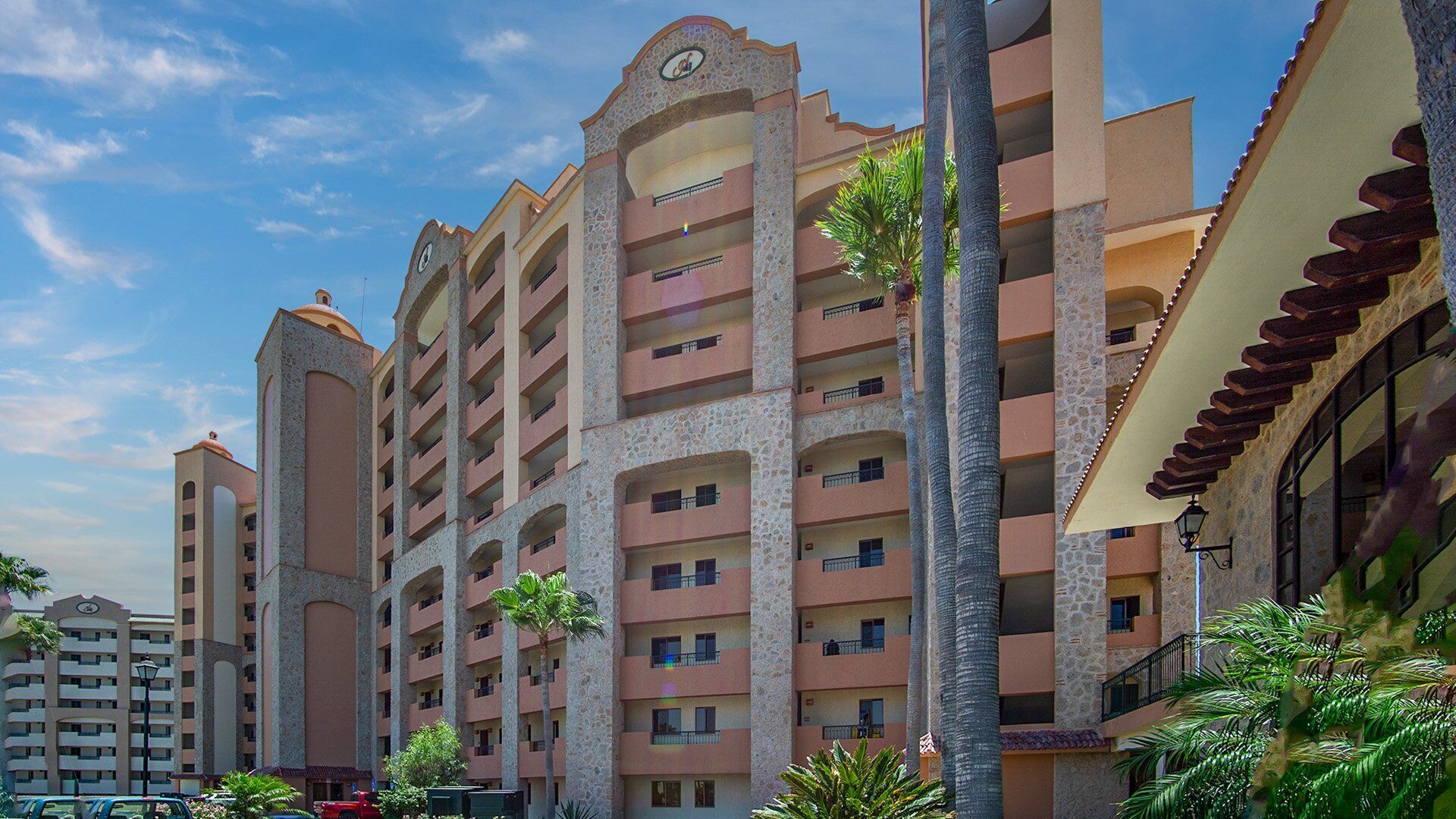 A multi-story hotel with balconies, a central courtyard, and palm trees.