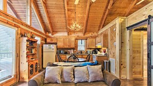 L’intérieur chaleureux d’un chalet avec un plafond en bois, un coin repas et un canapé agrémenté de coussins.