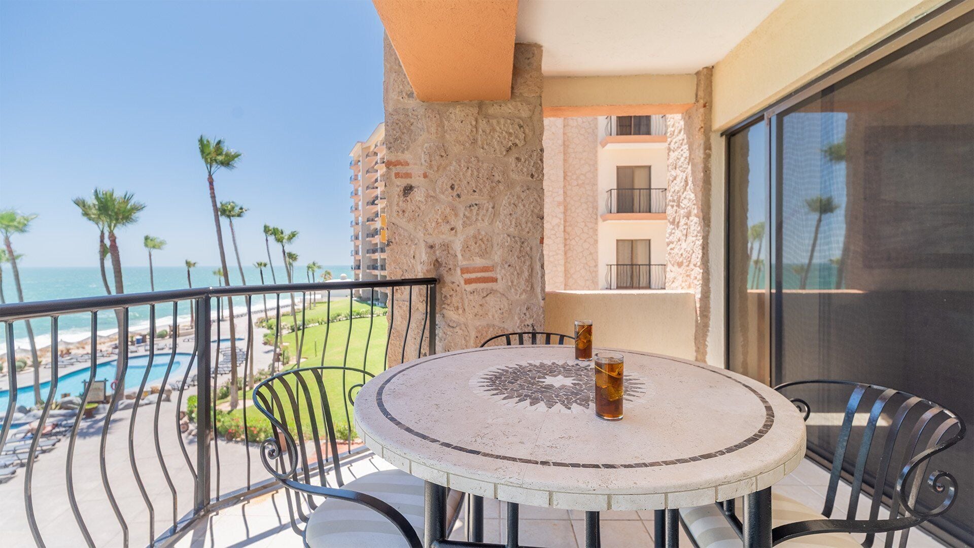 Un tavolo rotondo con sedie su un balcone che si affaccia su una piscina e una spiaggia.
