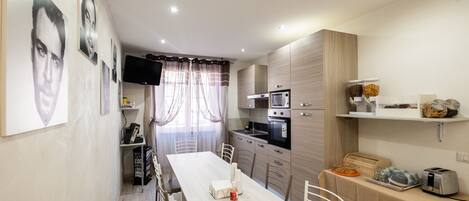 A modern kitchen with a dining area, featuring a long table, chairs, a microwave, oven, and a coffee machine.