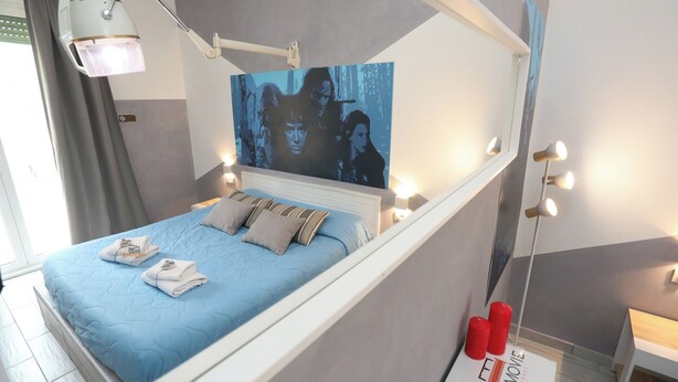 A bedroom with a bed, a painting, a nightstand, and a sign indicating a cinema room. - Cineroma Guesthouse (Rome)