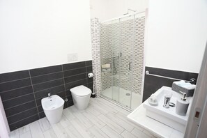 Ett modernt badrum med en duschavdelning med glasväggar, en bidé, en toalett och ett handfat med tillhörande hygienartiklar.