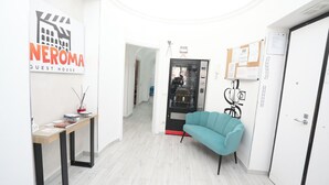 A modern hotel lobby with a reception desk, a teal armchair, and a glass door leading to a corridor. - Cineroma Guesthouse (Rome)