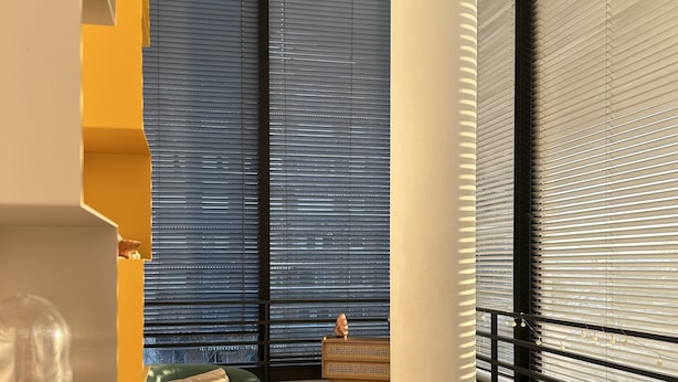 A modern living room with a green sofa, an orange chair, and a small table with a decorative item. Large windows with blinds are visible, and a staircase with yellow accents is in the background. - PARIS 12ème - 110 m² apartment near ARENA BERCY and Place DAUMESNIL (Paris)