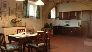 Un coin repas avec une table et des chaises en bois, une cuisine avec des meubles en bois et une arche en briques.