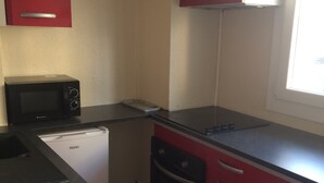 A compact kitchen with a microwave, a small refrigerator, and red cabinets. - Charming two room city center (Nice)