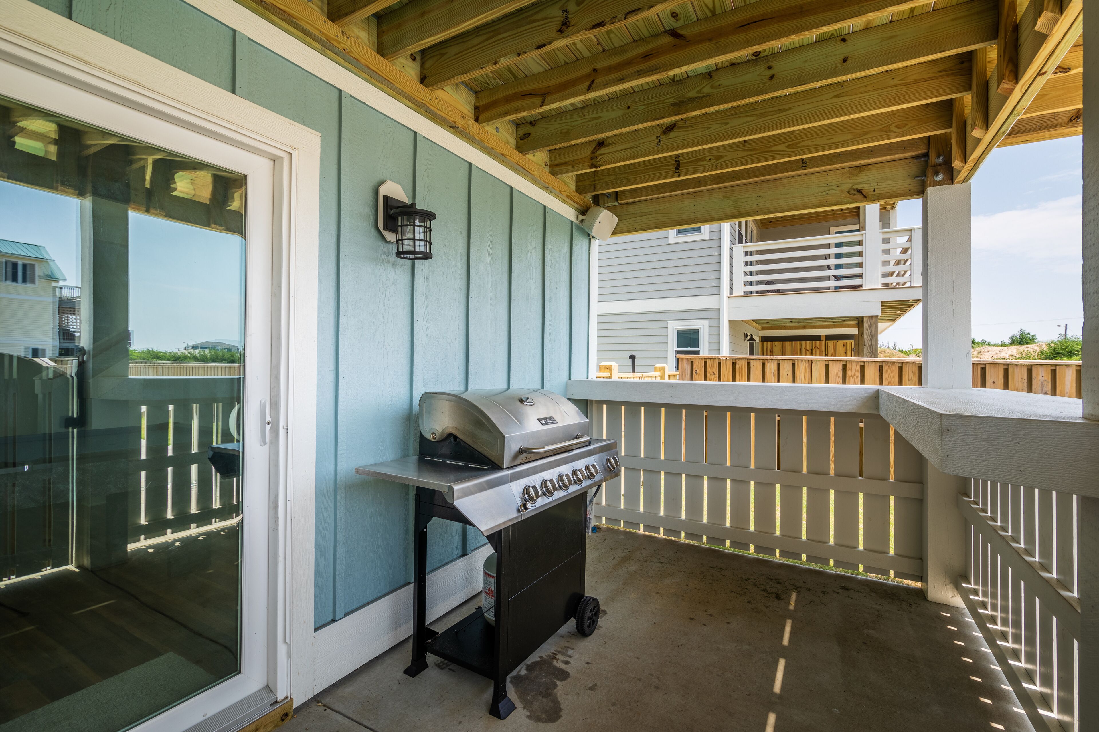 Une terrasse extérieure dotée d’un barbecue intégré et d’une porte vitrée donnant accès à un espace piscine.