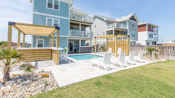 A multi-story residential building with a swimming pool, outdoor seating, and a wooden pergola. - 4746- Sandy Feet Retreat - Oceanside Kitty Hawk Retreat w/ Pool (Kitty Hawk)