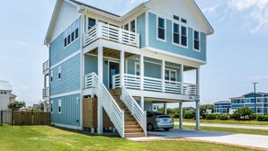 A two-story house with a covered front porch and a staircase leading to the upper level. - 4746- Sandy Feet Retreat - Oceanside Kitty Hawk Retreat w/ Pool (Kitty Hawk)