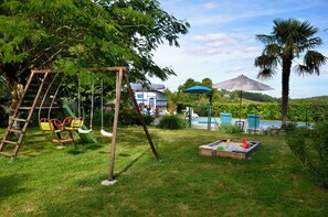 Ein Spielplatz mit Schaukeln und Rutsche, ein kleines Schwimmbecken und eine Palme.