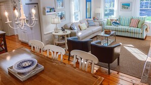 Een ruime woonkamer met een bank, stoelen, een salontafel en een eethoek met een tafel en stoelen.