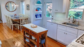 Une cuisine moderne avec des meubles blancs, un plan de travail en granit et un coin repas comprenant des chaises en bois et une table dressée pour quatre personnes.